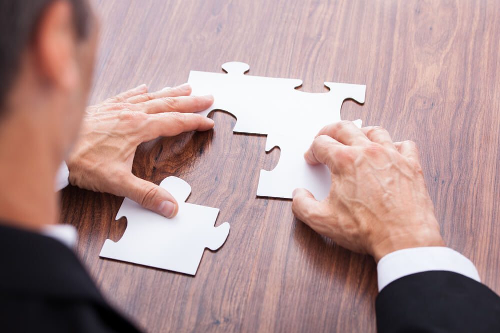 A person holding two pieces of puzzle on top of a table.